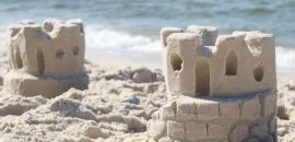 Two sandcastles sit on a sandy beach with the ocean water in the background