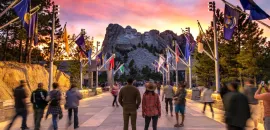People standing in a walkway looking at Mt. Rushmore, with flags on the sides.