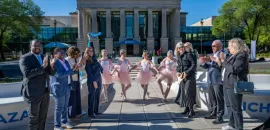 A crowd of people stand in front of a historic building, with ballet dancers, to celebrate cutting the ribbon.