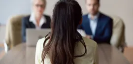 Image of two people interviewing a job candidate at a desk, with the candidate's back to the viewer.