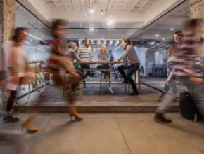 Four people sitting at a table and talking while people walk past.