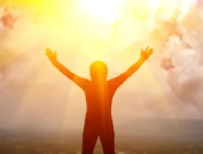 Image of person lifting arms with sun in the background.