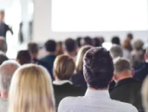 Photo of audience listening to speaker in conference center.