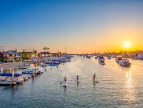 Photo of paddleboarders on Newport Harbor with sun setting in the distance.