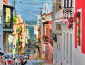 Photo of San Juan, Puerto Rico with colorful buildings on either side of a small street, with water in the background.