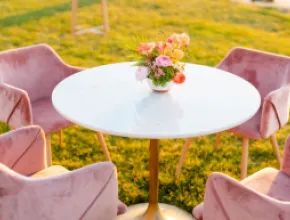 Photo of a pink table and chairs outside in a field of yellow flowers.