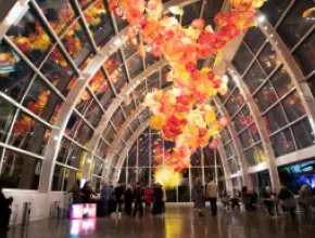 Photo of people gathered in a hall for Refract, under a glowing glass sculpture.