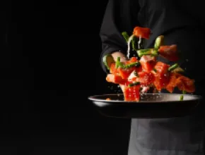 Image of chef flipping vegetables in a frying pan, with a black background.