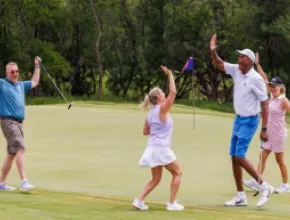 Photo of four people on a golf green, celebrating a good shot with two high-fiving.