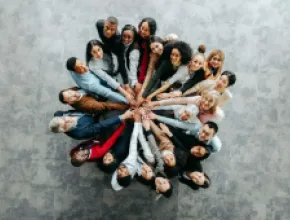 image of a bunch of people standing in a circle, with their extended hands touching in the center.
