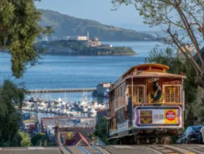 Photo of a cable car climbing a hill in San Francisco, with San Francisco Bay in the distance.