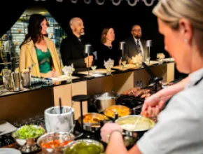 Photo of a chef preparing food in front of a small group of diners at an event.