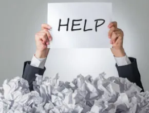 Image of a person holding a paper with the word HELP written on it, emerging from a bunch of crumpled up papers.