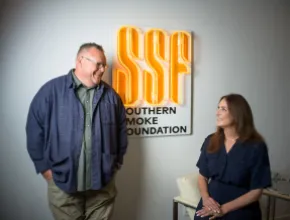 Photo of Chris Shepherd (left, standing) and Lindsay Brown (right sitting) in front of a Southern Smoke Foundation logo.