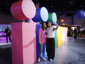 Two attendees take a selfie in front of the IMEX sign