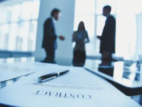 Photo of three people in the background with a contract in the forground.