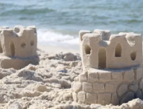 Two sandcastles sit on a sandy beach with the ocean water in the background