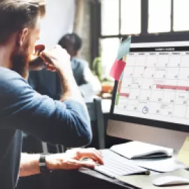 Man drinking water working on a computer with a calendar displayed on it.