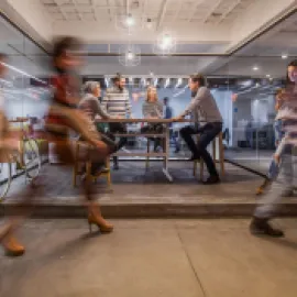 Four people sitting at a table and talking while people walk past.