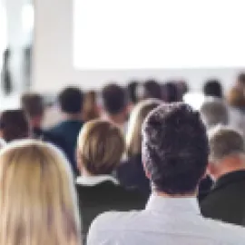 Photo of audience listening to speaker in conference center.