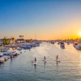 Photo of paddleboarders on Newport Harbor with sun setting in the distance.