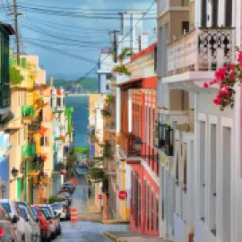 Photo of San Juan, Puerto Rico with colorful buildings on either side of a small street, with water in the background.