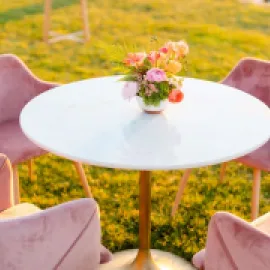 Photo of a pink table and chairs outside in a field of yellow flowers.