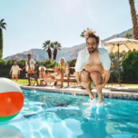 Photo of man jumping into a pool with a beach ball nearby.