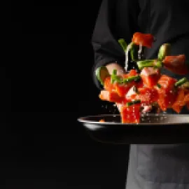 Image of chef flipping vegetables in a frying pan, with a black background.