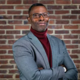 Photo of Elliott L. Ferguson II standing in front of a brick wall in a gray blazer.