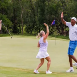 Photo of four people on a golf green, celebrating a good shot with two high-fiving.