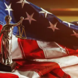 Photo of a model of Lady Liberty holding the Scales of Justice in front of an American flag.