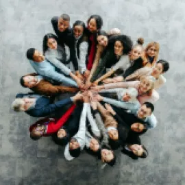 image of a bunch of people standing in a circle, with their extended hands touching in the center.
