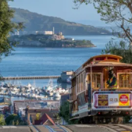 Photo of a cable car climbing a hill in San Francisco, with San Francisco Bay in the distance.