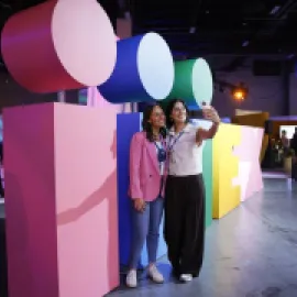 Two attendees take a selfie in front of the IMEX sign