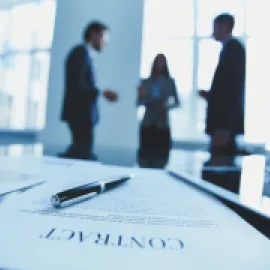 Photo of three people in the background with a contract in the forground.