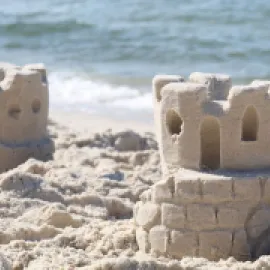 Two sandcastles sit on a sandy beach with the ocean water in the background