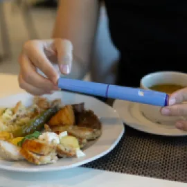 Image of a person with a GLP-1 injection pen next to a plate of food.