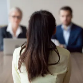 Image of two people interviewing a job candidate at a desk, with the candidate's back to the viewer.