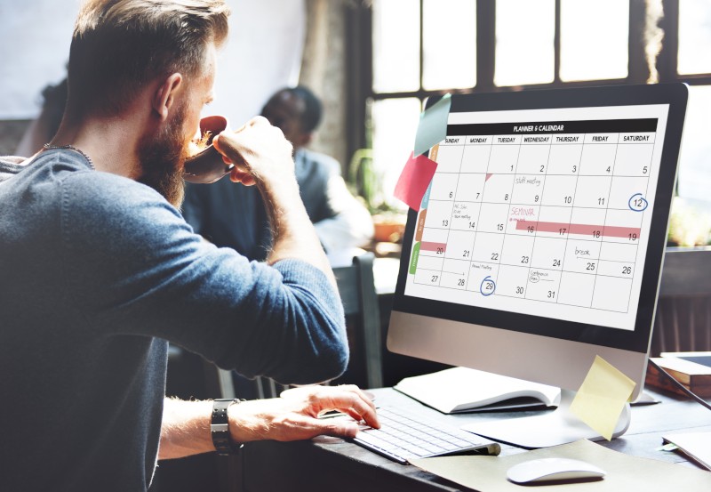 Man drinking water working on a computer with a calendar displayed on it.