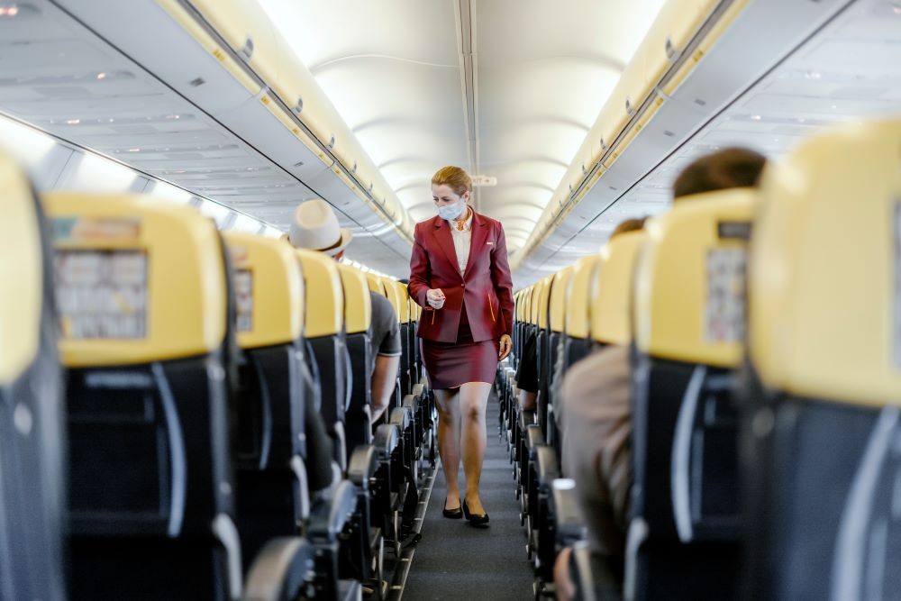 Masked flight attendant walking down airline aisle.