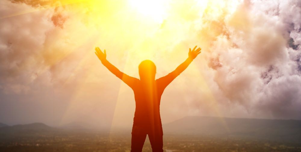 Image of person lifting arms with sun in the background.