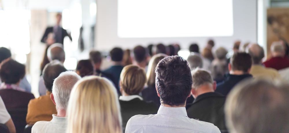 Photo of audience listening to speaker in conference center.