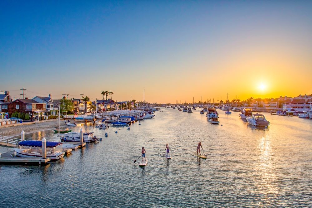 Photo of paddleboarders on Newport Harbor with sun setting in the distance.