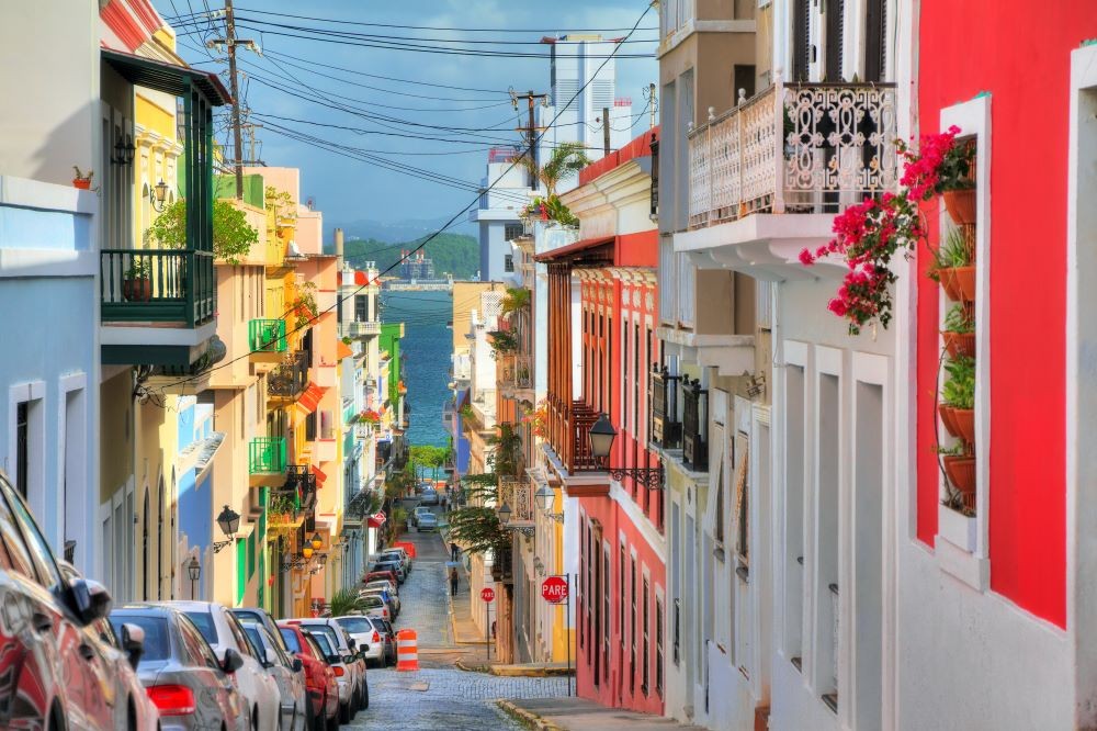 Photo of San Juan, Puerto Rico with colorful buildings on either side of a small street, with water in the background.