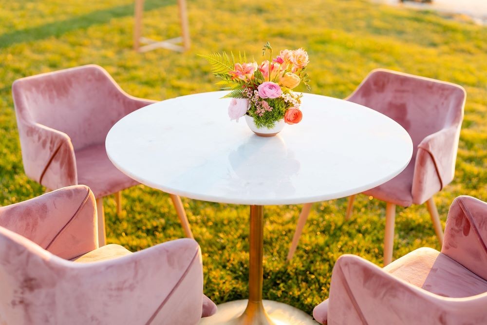 Photo of a pink table and chairs outside in a field of yellow flowers.