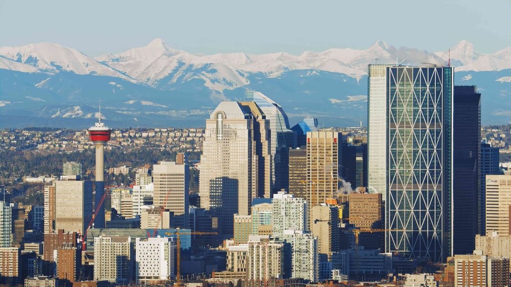 Photo of Calgary skyline with snow-capped mountains in the distance.