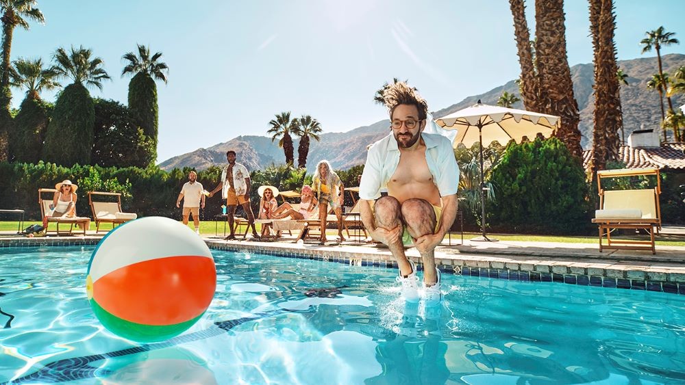 Photo of man jumping into a pool with a beach ball nearby.