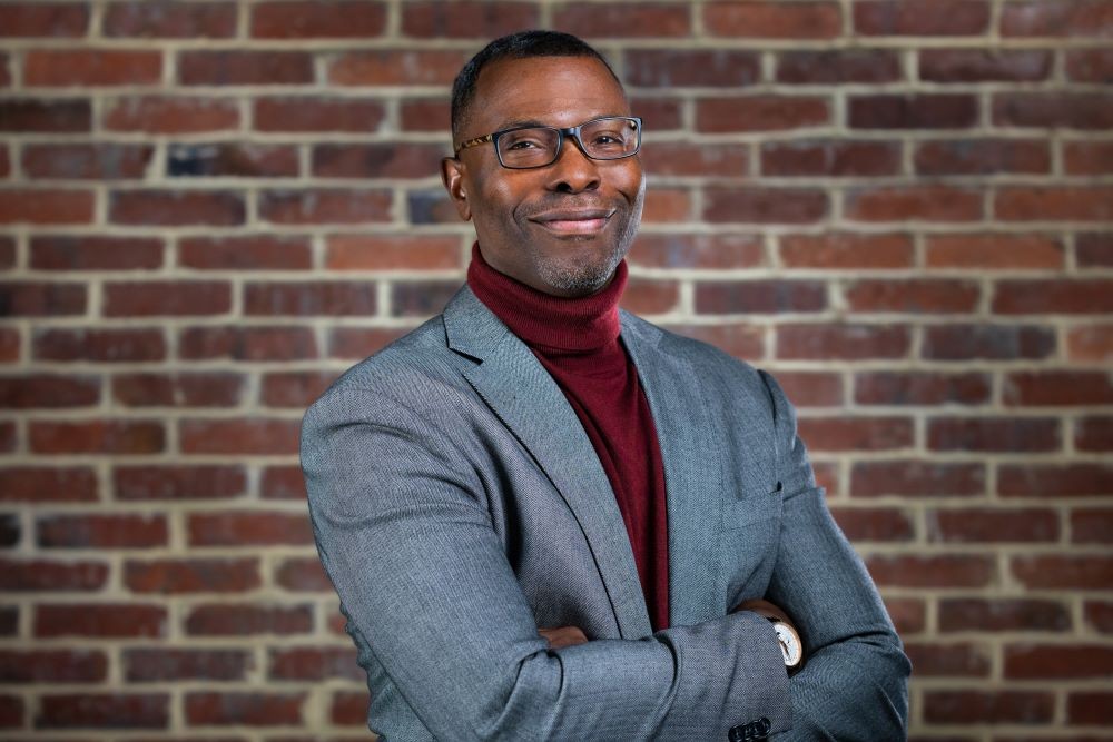 Photo of Elliott L. Ferguson II standing in front of a brick wall in a gray blazer.