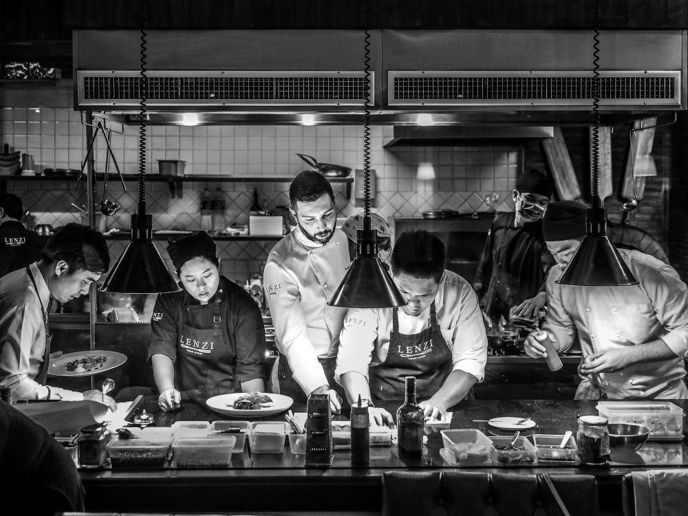 Black-and-white photo of a chef and assistants working in a kitchen.